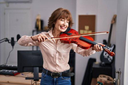 Foto de Mujer de mediana edad músico sonriendo confiado tocando violín en el estudio de música - Imagen libre de derechos