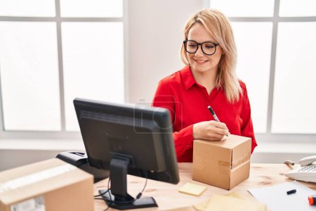 Photo for Young blonde woman ecommerce business worker writing on package at office - Royalty Free Image