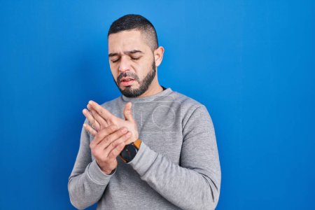Téléchargez les photos : Hispanic man standing over blue background suffering pain on hands and fingers, arthritis inflammation - en image libre de droit