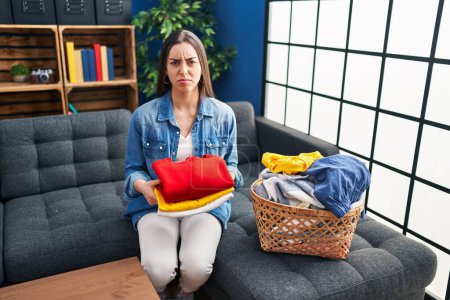 Foto de Hispanic woman holding folded laundry after ironing skeptic and nervous, frowning upset because of problem. negative person. - Imagen libre de derechos