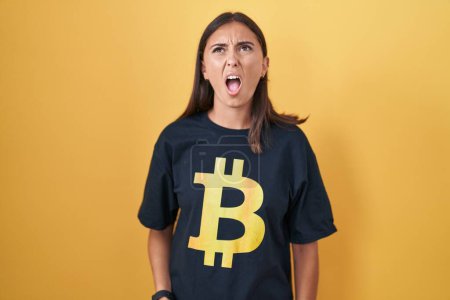 Téléchargez les photos : Jeune femme hispanique portant Bitcoin t-shirt en colère et fou hurlant frustré et furieux, criant de colère. rage et concept agressif. - en image libre de droit