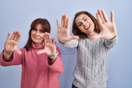 Téléchargez les photos : Mère et fille debout sur fond bleu faisant cadre en utilisant les mains paumes et les doigts, perspective de la caméra - en image libre de droit