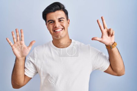 Foto de Hombre hispano de pie sobre fondo azul mostrando y señalando con los dedos número ocho mientras sonríe confiado y feliz. - Imagen libre de derechos