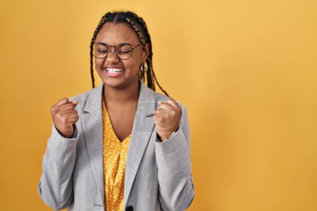 Téléchargez les photos : Femme afro-américaine avec des tresses debout sur fond jaune excité pour le succès avec les bras levés et les yeux fermés célébrant la victoire en souriant. concept gagnant. - en image libre de droit