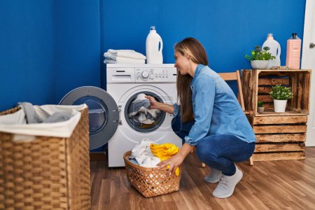 Foto de Joven mujer rubia sonriendo confiado lavado de ropa en la lavandería - Imagen libre de derechos