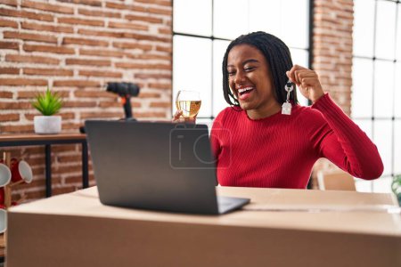 Photo for Young african american with braids showing keys of new home doing video call smiling and laughing hard out loud because funny crazy joke. - Royalty Free Image