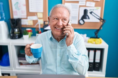 Téléchargez les photos : Moyen âge homme aux cheveux gris homme d'affaires parler sur smartphone boire du café au bureau - en image libre de droit