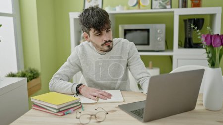 Téléchargez les photos : Jeune homme hispanique étudiant utilisant l'ordinateur prenant des notes à la salle à manger - en image libre de droit