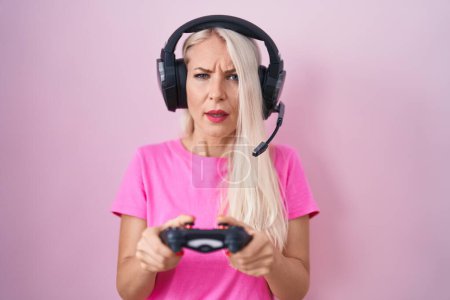 Foto de Mujer caucásica jugando videojuego sosteniendo controlador expresión despistada y confusa. concepto de duda. - Imagen libre de derechos