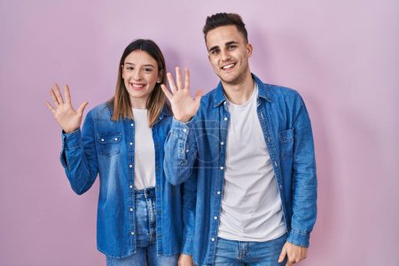 Téléchargez les photos : Jeune couple hispanique debout sur fond rose montrant et pointant vers le haut avec les doigts numéro dix tout en souriant confiant et heureux. - en image libre de droit