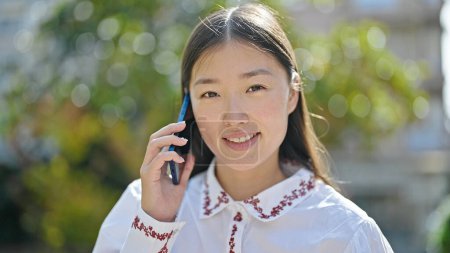 Téléchargez les photos : Jeune femme chinoise parlant sur smartphone souriant au parc - en image libre de droit
