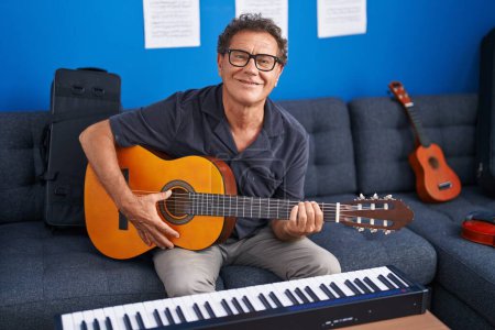 Foto de Middle age man musician playing classical guitar at music studio - Imagen libre de derechos