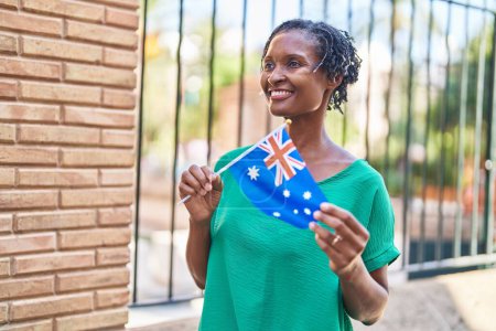 Téléchargez les photos : Moyen âge femme afro-américaine souriante confiante tenant drapeau australie à la rue - en image libre de droit
