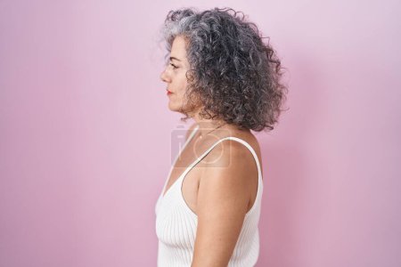 Photo for Middle age woman with grey hair standing over pink background looking to side, relax profile pose with natural face and confident smile. - Royalty Free Image