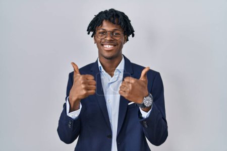 Téléchargez les photos : Jeune homme africain avec dreadlocks veste d'affaires sur fond blanc signe de succès faire geste positif avec la main, pouces levés souriant et heureux. expression joyeuse et geste gagnant. - en image libre de droit