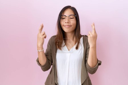 Photo for Middle age chinese woman wearing glasses over pink background gesturing finger crossed smiling with hope and eyes closed. luck and superstitious concept. - Royalty Free Image