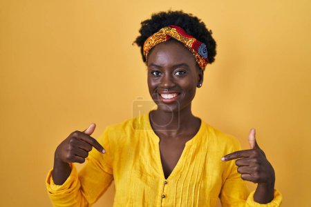 Téléchargez les photos : Jeune femme africaine portant turban africain regardant confiant avec le sourire sur le visage, se montrant du doigt fier et heureux. - en image libre de droit