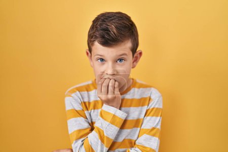 Photo for Young caucasian kid standing over yellow background looking stressed and nervous with hands on mouth biting nails. anxiety problem. - Royalty Free Image