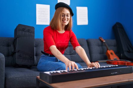 Foto de Joven pelirroja músico sonriendo confiado tocando el piano en el estudio de música - Imagen libre de derechos