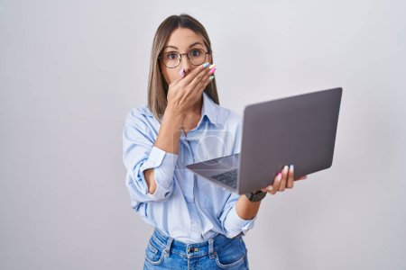 Téléchargez les photos : Jeune femme travaillant à l'aide d'un ordinateur portable choqué couvrant la bouche avec les mains pour erreur. concept secret. - en image libre de droit