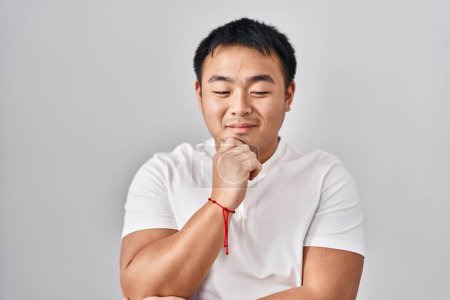 Photo for Young chinese man standing over white background with hand on chin thinking about question, pensive expression. smiling with thoughtful face. doubt concept. - Royalty Free Image
