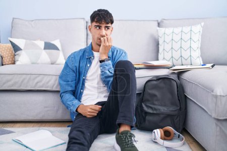 Photo for Young hispanic man sitting on the floor studying for university looking stressed and nervous with hands on mouth biting nails. anxiety problem. - Royalty Free Image