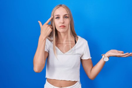 Photo for Young caucasian woman standing over blue background confused and annoyed with open palm showing copy space and pointing finger to forehead. think about it. - Royalty Free Image