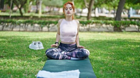Foto de Joven pelirroja entrenando yoga ejercicio sentado sobre hierba en el parque - Imagen libre de derechos