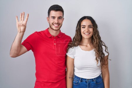 Foto de Joven pareja hispana de pie sobre un fondo aislado mostrando y señalando hacia arriba con los dedos número cuatro mientras sonríe confiada y feliz. - Imagen libre de derechos