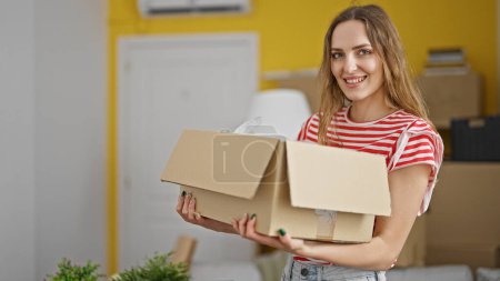 Téléchargez les photos : Young blonde woman smiling confident holding package at new home - en image libre de droit