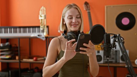 Foto de Joven mujer rubia músico con auriculares cantando canción en el estudio de música - Imagen libre de derechos