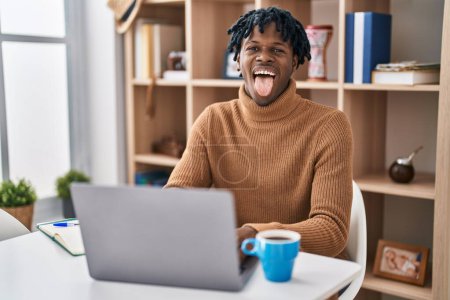 Photo for Young african man with dreadlocks working using computer laptop sticking tongue out happy with funny expression. emotion concept. - Royalty Free Image