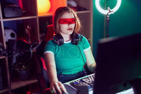 Foto de Mujer pelirroja joven streamer jugando videojuego utilizando gafas de realidad virtual en la sala de juegos - Imagen libre de derechos