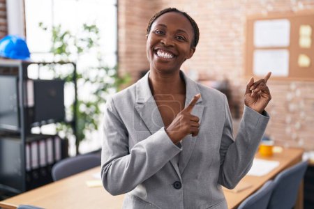 Photo for African american woman at the office smiling and looking at the camera pointing with two hands and fingers to the side. - Royalty Free Image