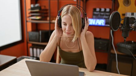 Foto de Mujer joven rubia reportera de radio escuchando música en podcast studio - Imagen libre de derechos