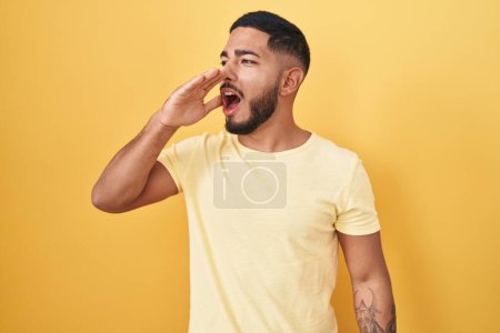Photo for Young hispanic man standing over yellow background shouting and screaming loud to side with hand on mouth. communication concept. - Royalty Free Image