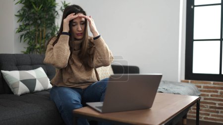 Photo for Beautiful hispanic woman using laptop sitting on sofa with worried expression at home - Royalty Free Image