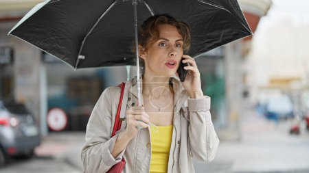 Téléchargez les photos : Jeune femme tenant parapluie parler sur smartphone à la rue - en image libre de droit