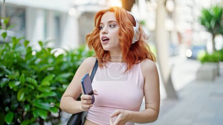 Téléchargez les photos : Jeune rousse femme écouter de la musique souriant à la rue - en image libre de droit