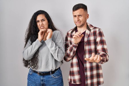Photo for Young hispanic couple standing over white background disgusted expression, displeased and fearful doing disgust face because aversion reaction. - Royalty Free Image