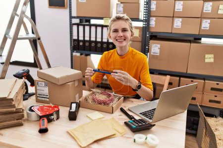 Téléchargez les photos : Jeune femme blonde ecommerce travailleur d'affaires faire la photo au diadème sur la boîte en carton au bureau - en image libre de droit