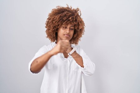 Photo for Young hispanic woman with curly hair standing over white background punching fist to fight, aggressive and angry attack, threat and violence - Royalty Free Image