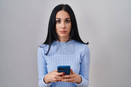 Photo for Hispanic woman using smartphone relaxed with serious expression on face. simple and natural looking at the camera. - Royalty Free Image
