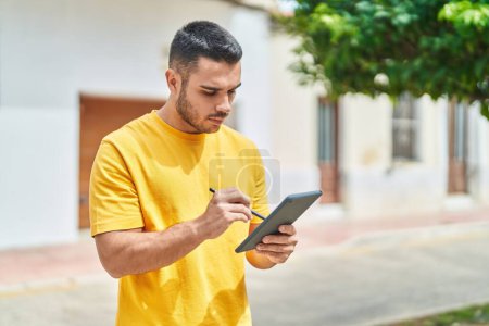 Photo for Young hispanic man drawing on touchpad with serious expression at street - Royalty Free Image