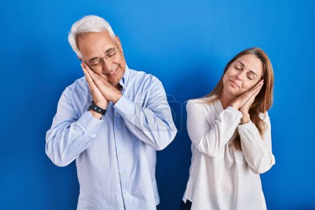 Téléchargez les photos : Couple hispanique du moyen âge debout sur fond bleu endormi fatigué rêvant et posant les mains ensemble tout en souriant les yeux fermés. - en image libre de droit