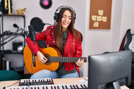 Téléchargez les photos : Jeune belle musicienne hispanique jouant de la guitare classique au studio de musique - en image libre de droit