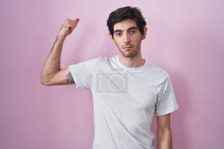 Foto de Joven hombre hispano de pie sobre fondo rosa fuerte persona mostrando el músculo del brazo, confiado y orgulloso de poder - Imagen libre de derechos