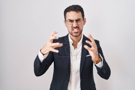 Téléchargez les photos : Beau homme d'affaires hispanique debout sur fond blanc criant frustré par la rage, mains essayant d'étrangler, hurlant fou - en image libre de droit