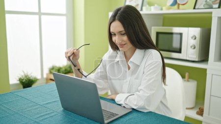 Photo for Young beautiful hispanic woman using laptop sitting on table at dinning room - Royalty Free Image