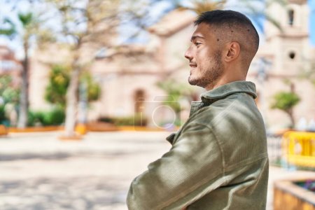 Téléchargez les photos : Jeune homme hispanique souriant confiant debout avec les bras croisés geste au parc - en image libre de droit